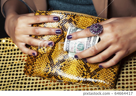 pretty fingers of african american woman holding money closeup with purse, luxury jewellery on python clutch, cash for gifts 64664417