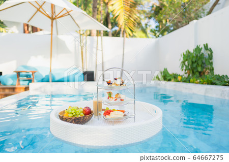 Breakfast and afternoon tea set floating around swimming pool Breakfast and afternoon tea set floating around swimming pool 64667275