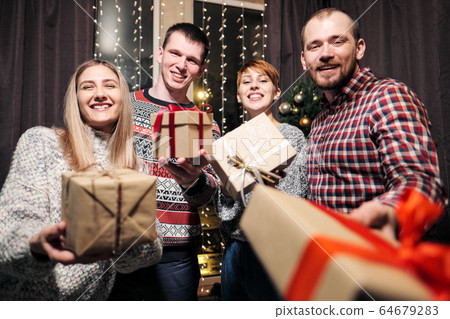 A group of friends, men and women, celebrate Christmas. They give each other presents, rejoice and laugh. New Years Eve. A group of friends, men and women, celebrate Christmas. They give each other presents, rejoice and laugh. New Years Eve. 64679283