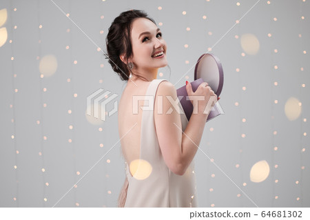 Young brunette woman in evening dress on a white background. Holding Christmas present box. Joy, happiness and surprise. Young brunette woman in evening dress on a white background. Holding Christmas present box. Joy, happiness and surprise. 64681302