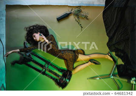 Fashion photo session in the studio. Beautiful woman model. Yellow leopard dress. Studio racks and flashes. Yellow and green background. Fashion photo session in the studio. Beautiful woman model. Yellow leopard dress. Studio racks and flashes. Yellow and green background. 64681342