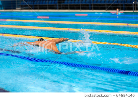 Athletic man swimming in butterfly style in the swimming pool with clear blue water. 64684146