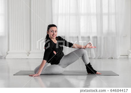 Beautiful asian young woman practicing yoga. Happy and smiling during workout, doing variation of yoga asana on gray mat 64684417