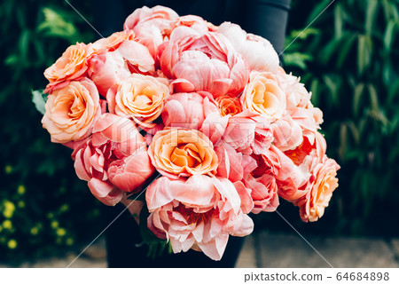 Woman in black dress is holding bunch of pink peonies and roses 64684898