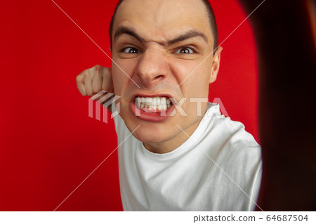Caucasian young man's portrait on red studio background, emotinal and expressive Caucasian young man's portrait on red studio background, emotinal and expressive 64687504