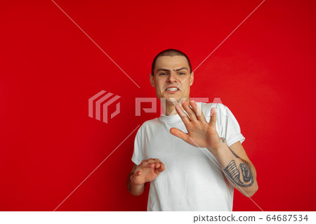 Caucasian young man's portrait on red studio background, emotinal and expressive 64687534