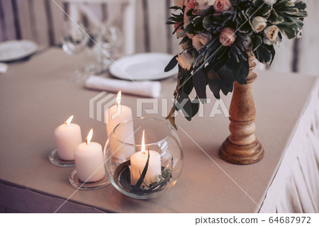 A table with a bouquet of flowers in a vase and lit candles A table with a bouquet of flowers in a vase and lit candles 64687972