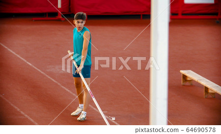 Pole vault training on the stadium - a young man preparing before the jump Pole vault training on the stadium - a young man preparing before the jump 64690578