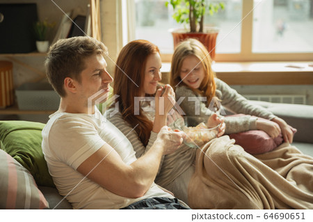 Family spending nice time together at home, looks happy and cheerful, watching TV 64690651