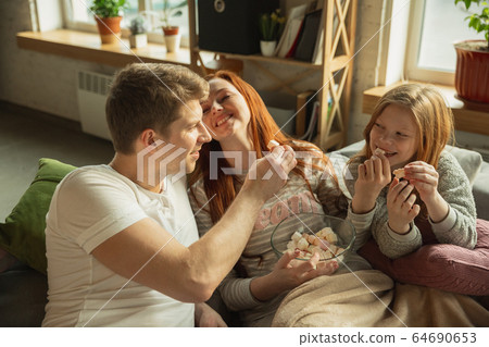 Family spending nice time together at home, looks happy and cheerful, watching TV Family spending nice time together at home, looks happy and cheerful, watching TV 64690653
