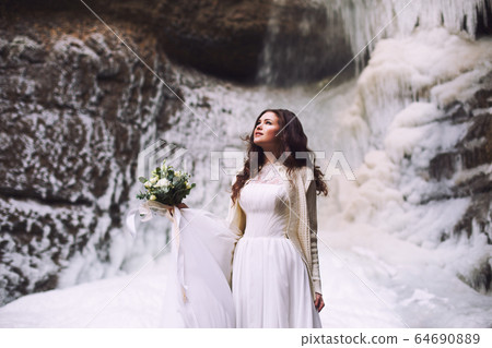 Bride with a bouquet of flowers and a wedding dress on a background of a glacier in the mountains Bride with a bouquet of flowers and a wedding dress on a background of a glacier in the mountains 64690889