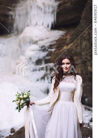 Bride in wedding dress with bouquet in front of glacier 64690917