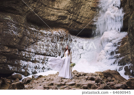 Beautiful girl in a wedding dress with a bouquet of flowers on a background of mountains Beautiful girl in a wedding dress with a bouquet of flowers on a background of mountains 64690945