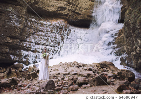 A girl in a wedding dress with a bouquet of flowers on a background of a glacier 64690947