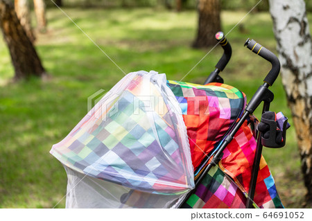 Child in stroller covered with protective net during walk. Baby carriage with anti-mosquito white cover. Midge protection for children during outdoor walking season 64691052
