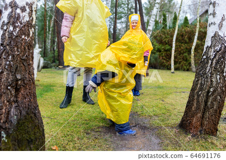 Mother with cute adorable caucasian siblings children in bright yellow raincoat and wellies playing at garden during cold spring rainy day at home backyard. Carefree childhood concept. Bad weather Mother with cute adorable caucasian siblings children in bright yellow raincoat and wellies playing at garden during cold spring rainy day at home backyard. Carefree childhood concept. Bad weather 64691176