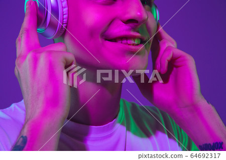 Caucasian man's portrait isolated on purple studio background in neon light 64692317