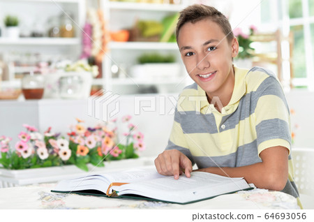 Smiling boy reading a book at the table 64693056