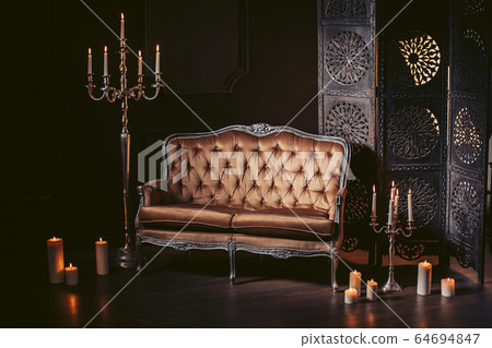 Luxurious sofa in a modern interior, decorated with decor and candles. In dark tones and gold Luxurious sofa in a modern interior, decorated with decor and candles. In dark tones and gold 64694847