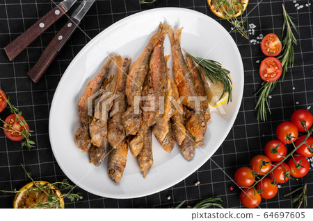 A dish of fried red mullet. Table setting, decorated with greens and cherry tomatoes. 64697605
