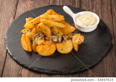 Fried potato wedges on a round black board with mustard sauce. 64697614