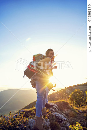 Hikers with backpacks relaxing on top of a mountain and enjoying the view of valley 64699589