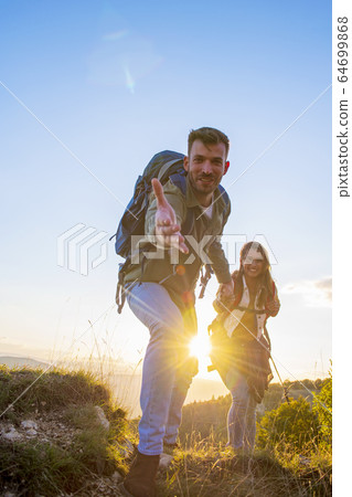 People helping each other hike up a mountain at sunrise. People helping each other hike up a mountain at sunrise. 64699868