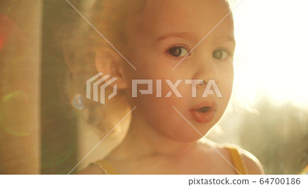 Surprised blonde baby girl at window against blazing sun Surprised blonde baby girl at window against blazing sun 64700186