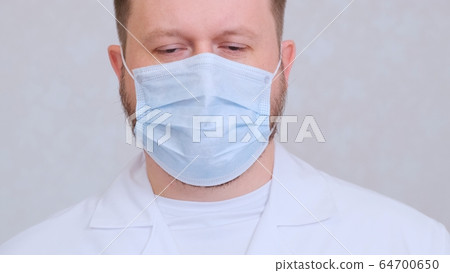 sad and upset Male in a protective mask and a white shirt looks at the camera, close-up. Hygiene sad and upset Male in a protective mask and a white shirt looks at the camera, close-up. Hygiene 64700650