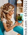 girl in a luxurious white dress sitting on a soft armchair holds in her hands green flower in a pot 64702022