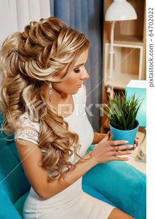 girl in a luxurious white dress sitting on a soft armchair holds in her hands green flower in a pot girl in a luxurious white dress sitting on a soft armchair holds in her hands green flower in a pot 64702022