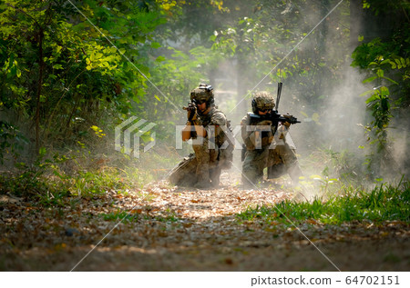 Two soldiers with the fighting uniform sit on the ground and point gun to target Two soldiers with the fighting uniform sit on the ground and point gun to target 64702151