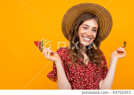 girl in a straw hat and a red summer dress with candy in hand on a yellow isolated background 64702953