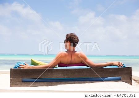 Relaxed man in luxury lounger enjoying summer vacations on beautiful beach. 64703351