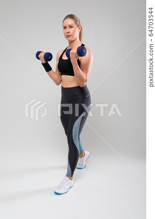 slim fit blonde girl in a sports uniform is engaged in physical exercises on a gray background 64703544