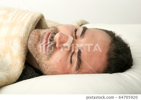 Man sleeping in bed using a nasal strip. 64705920
