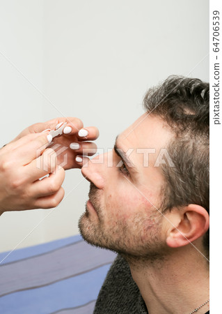 Female helping her boyfriend to put a nasal strip on his nose Female helping her boyfriend to put a nasal strip on his nose 64706539