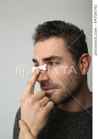 Man holding a nasal strip on his nose Man holding a nasal strip on his nose 64706542