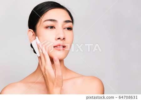 young beautiful asian woman with clean and bright skin, Cosmetic Beauty Concept,hands touch on the cheek, smiling and friendly face isolated on grey background 64708631