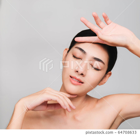 young beautiful asian woman with clean and bright skin, Cosmetic Beauty Concept,hands touch on the cheek, smiling and friendly face isolated on grey background 64708633