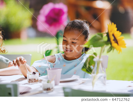 Small girl sitting outdoors in garden in summer, eating snacks. 64712762