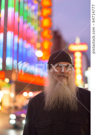 Mature bearded tourist man with eyeglasses thinking in Chinatown at night 64714777