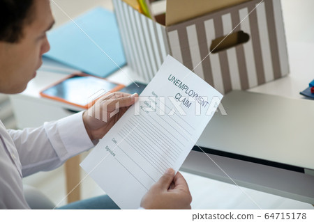Young brunette male sitting at his desk, holding unemployment claim 64715178