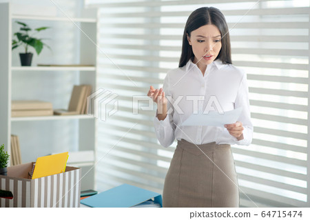 Upset young brunette female holding piece of paper, reading it 64715474