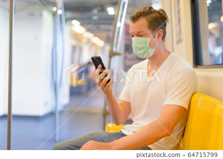 Young man using phone inside the train with mask for protection from corona virus outbreak 64715799
