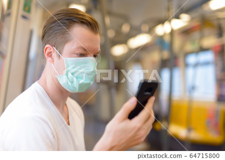 Young man using phone and wearing mask for protection from corona virus outbreak inside the train 64715800