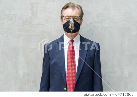 Mature businessman in suit with mask for protection from corona virus outbreak against concrete wall Mature businessman in suit with mask for protection from corona virus outbreak against concrete wall 64715863