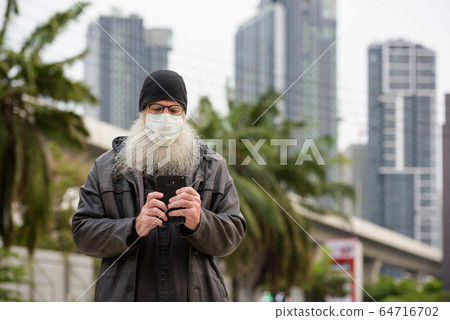 Mature bearded hipster man with mask using phone outdoors Mature bearded hipster man with mask using phone outdoors 64716702