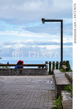 Backpack with red rain cover and walking sticks. Waiting for opening a hostel. Way of St. James, Basque Country, Spain. Camino de Santiago. 64717674