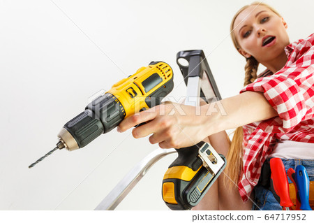 Woman using drill on ladder 64717952
